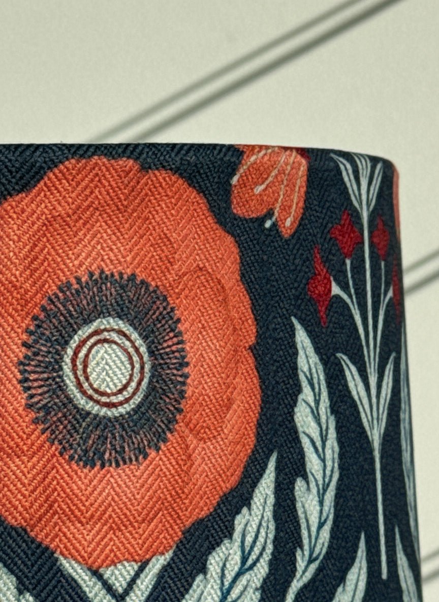 Close-up of a fabric with floral pattern lampshade featuring orange flowers and green leaves on a dark blue background.