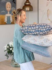 Woman holding floral-patterned pillows in a room with decorative elements.