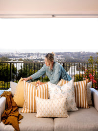 Woman arranging pillows on a sofa with a scenic view in the background