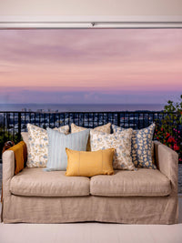 Beige sofa with patterned cushions against a scenic backdrop of a sunset over water.