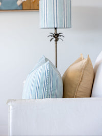 Decorative lamp with striped shade next to pillows on a sofa against a white wall.