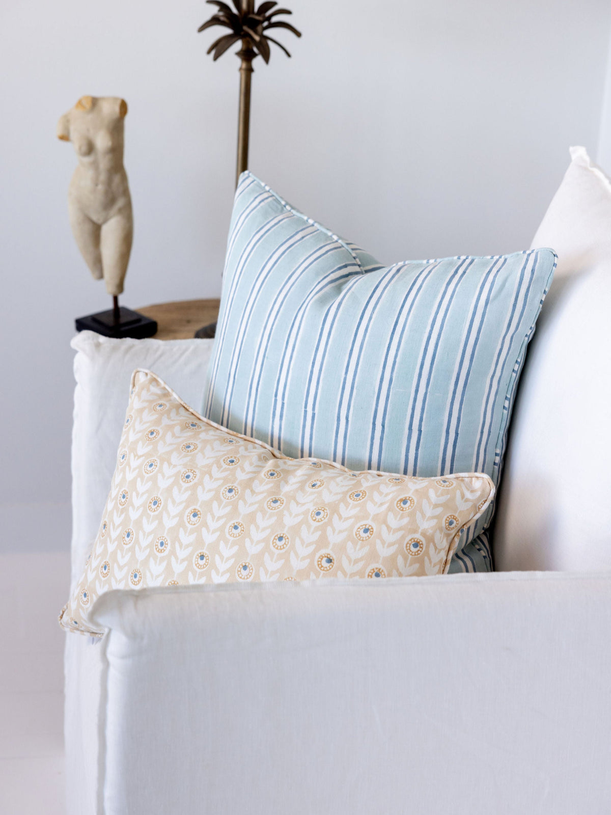 Light blue striped pillow and beige patterned pillow on a white sofa with a lamp and decorative object in the background.
