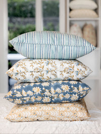 Stack of decorative pillows with floral and striped patterns on a bed.