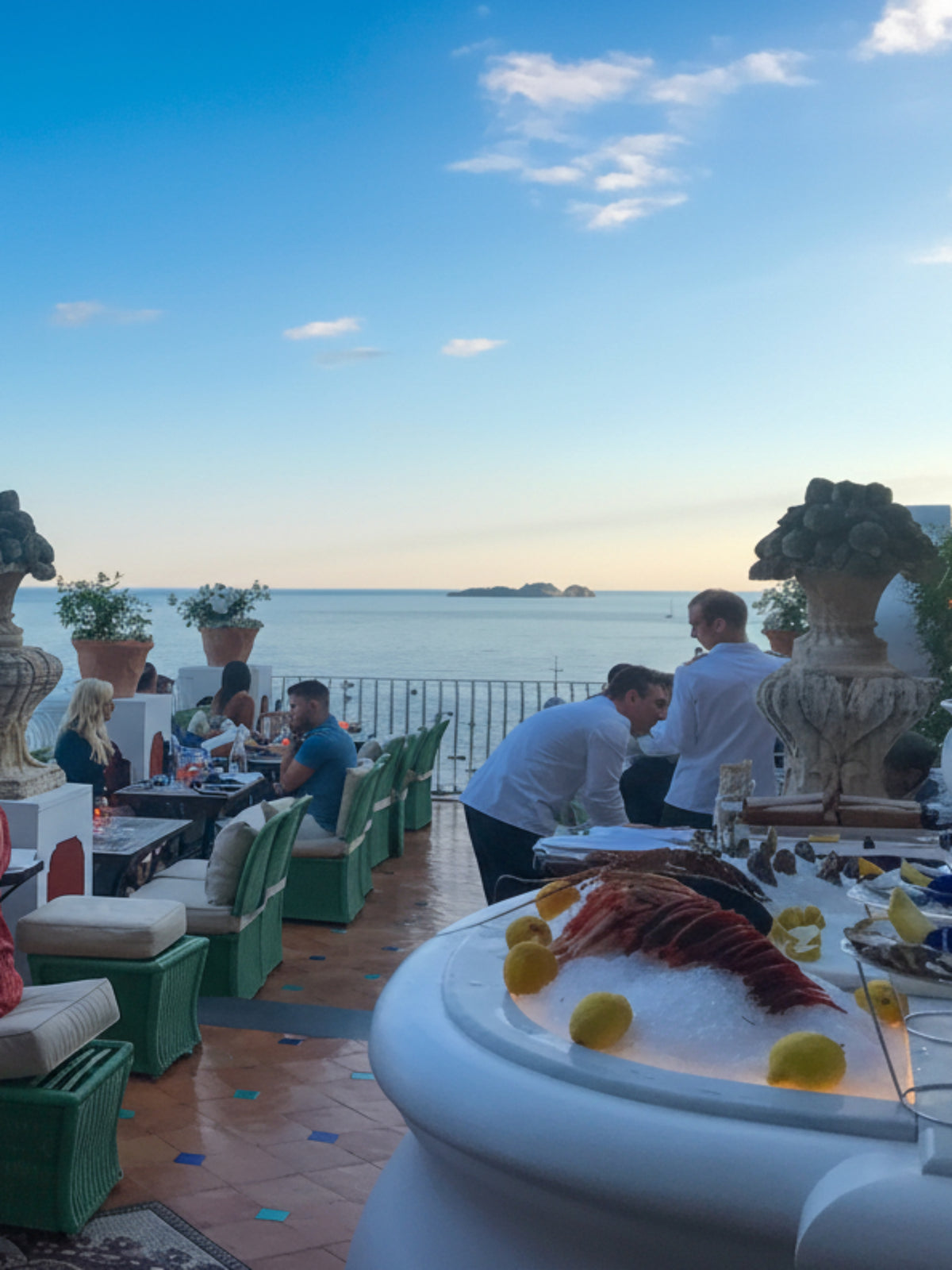 People enjoying a meal on a rooftop with ocean view during sunset.