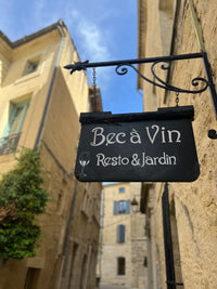 Sign for 'Bec a Vin Resto & Jardin' hanging against a building exterior.