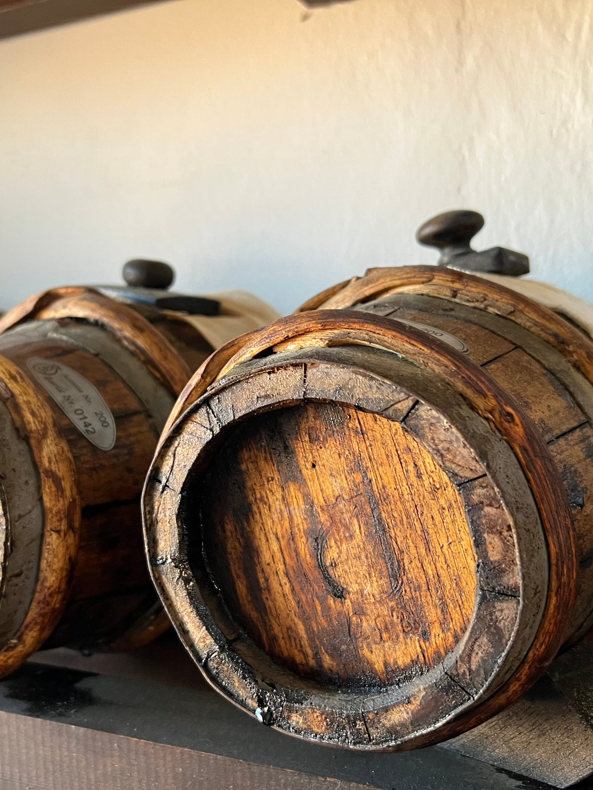 Three wooden barrels with metal lids on a wooden shelf.