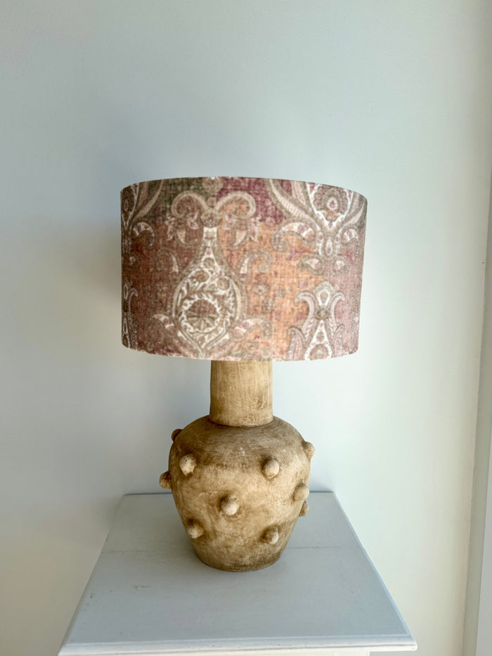 Decorative lamp with a patterned shade on a white surface against a light gray wall