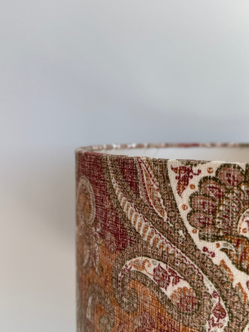 Close-up of a cylindrical fabric product with intricate paisley pattern on a light gray background