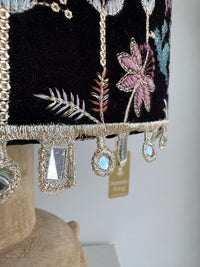 Decorative pillow with floral embroidery and beaded trim on a neutral background