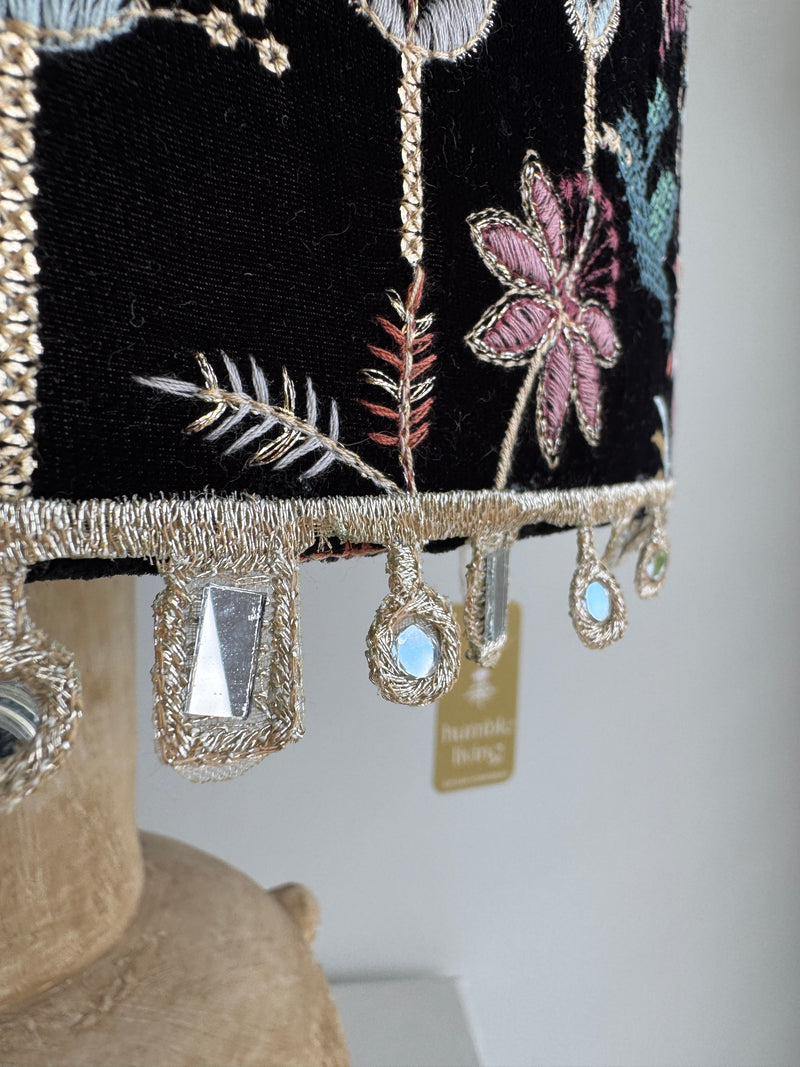 Decorative pillow with floral embroidery and beaded trim on a neutral background