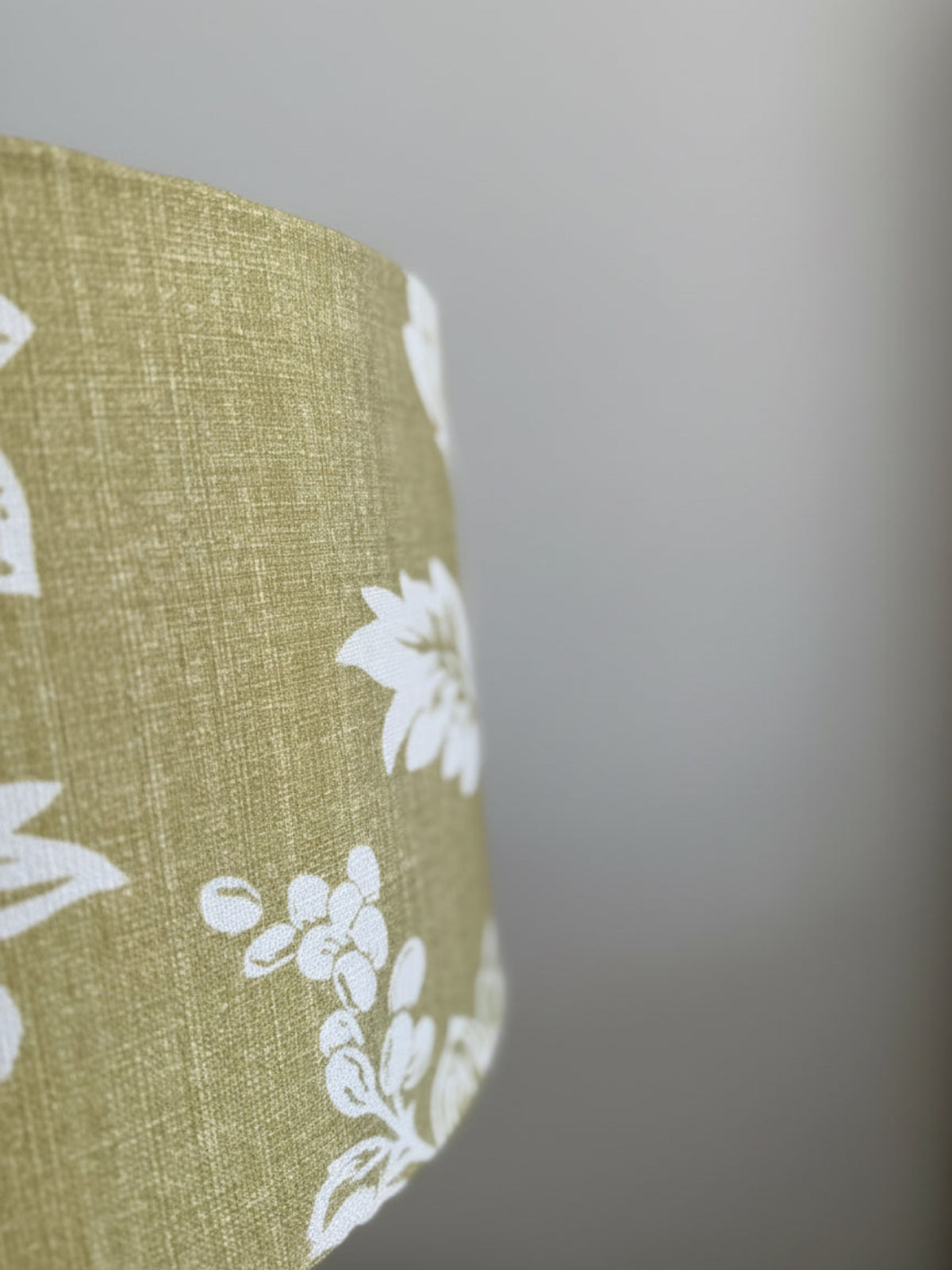 Close-up of a green fabric lampshade with white floral patterns on a blurred background