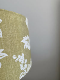 Close-up of a green fabric lampshade with white floral patterns on a blurred background