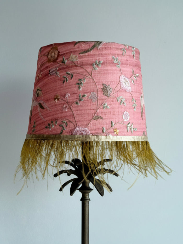 Lamp with a pink floral lampshade and gold fringe on a plain background