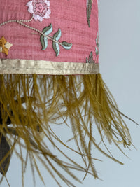 Decorative fabric with floral embroidery and feathered trim on a plain background