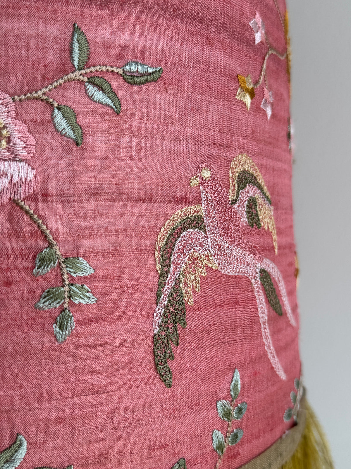 Embroidered fabric with floral and bird patterns on a pink background