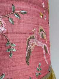 Embroidered fabric with floral and bird patterns on a pink background