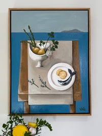 Framed artwork of a still life scene with a fish, lemon, and other elements on a table.