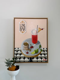 Framed artwork of a cocktail with a geometric pattern on a wall.