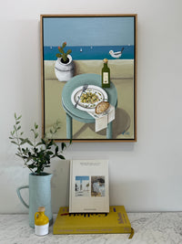 Framed artwork on a wall with books and a plant below