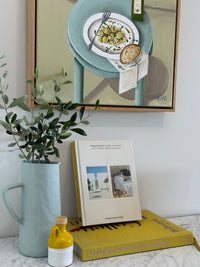 Framed artwork of a plate with food, book, and green plant on a surface.