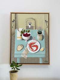 Framed artwork of a table setting with food and decor on a white wall.