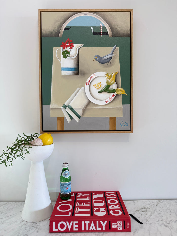 Framed still life painting on a wall above a red book titled 'Love Italy'.