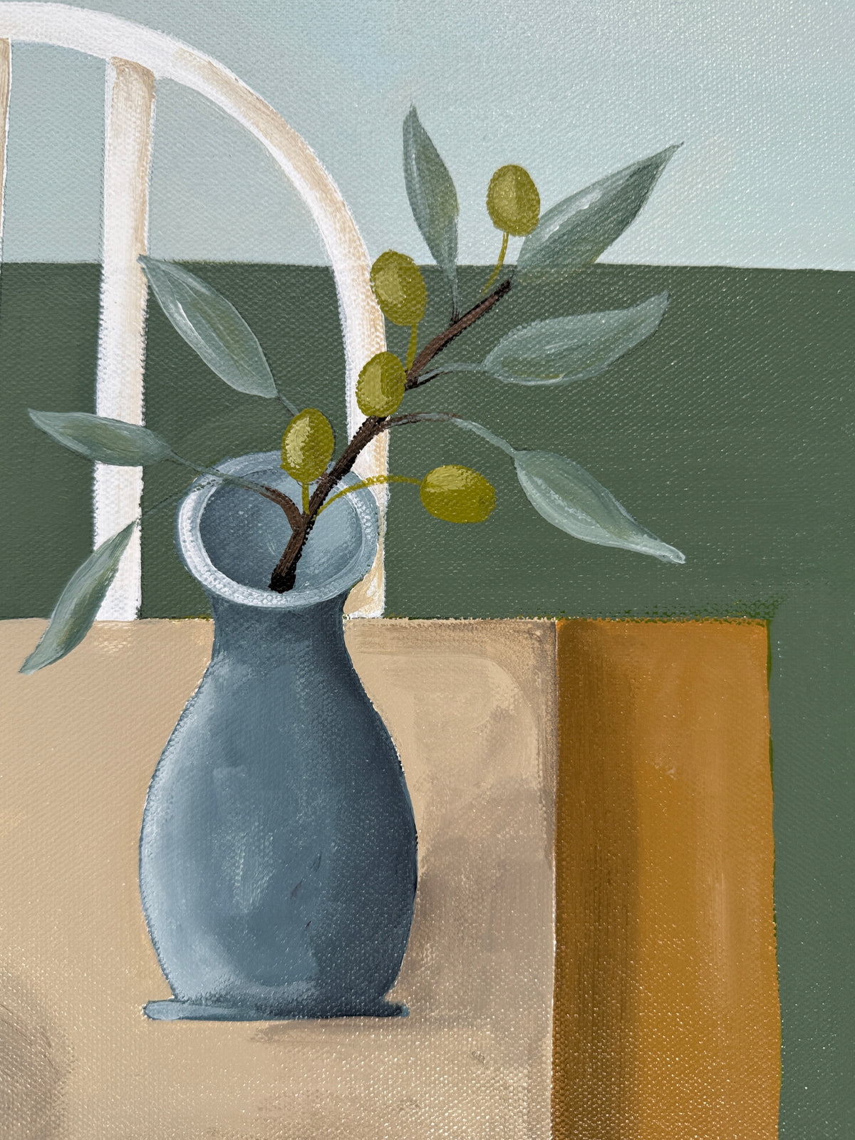 Gray vase with green branch and leaves on a textured surface with a chair and wall in the background