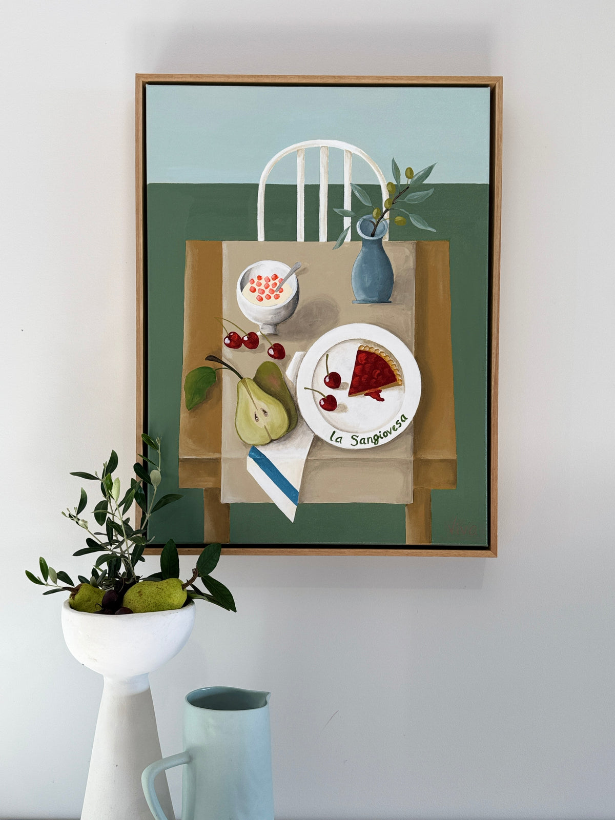 Framed artwork of a still life scene with a table setting on a wall.