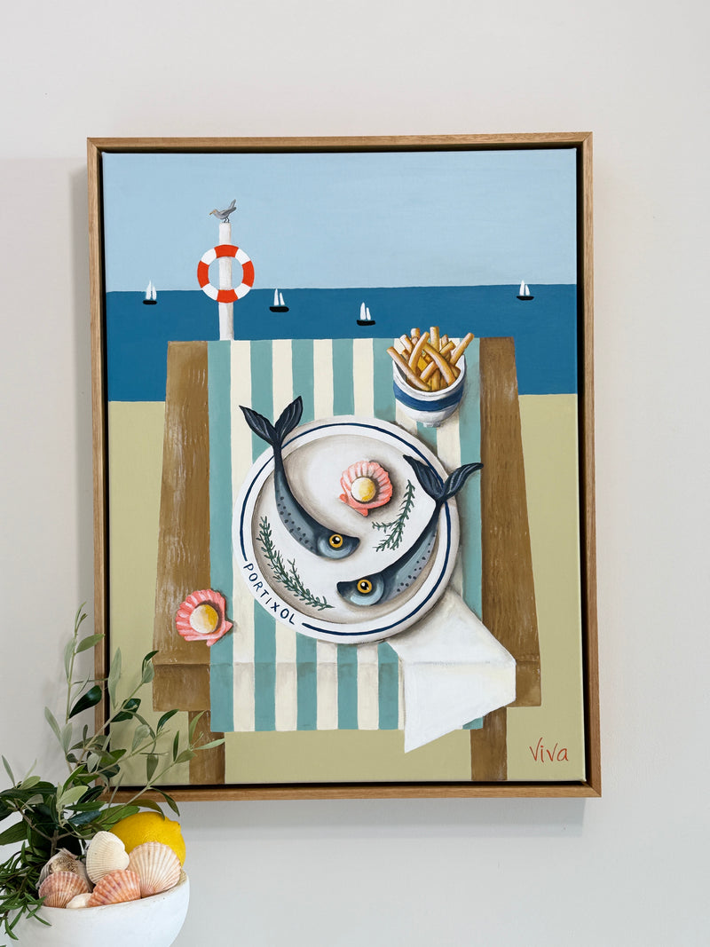 Framed artwork with a nautical theme featuring fish, a plate, and a life buoy on a beach setting.