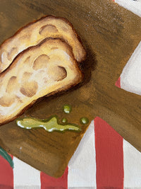Close-up of a piece of bread with a green spread on a wooden board with a striped background