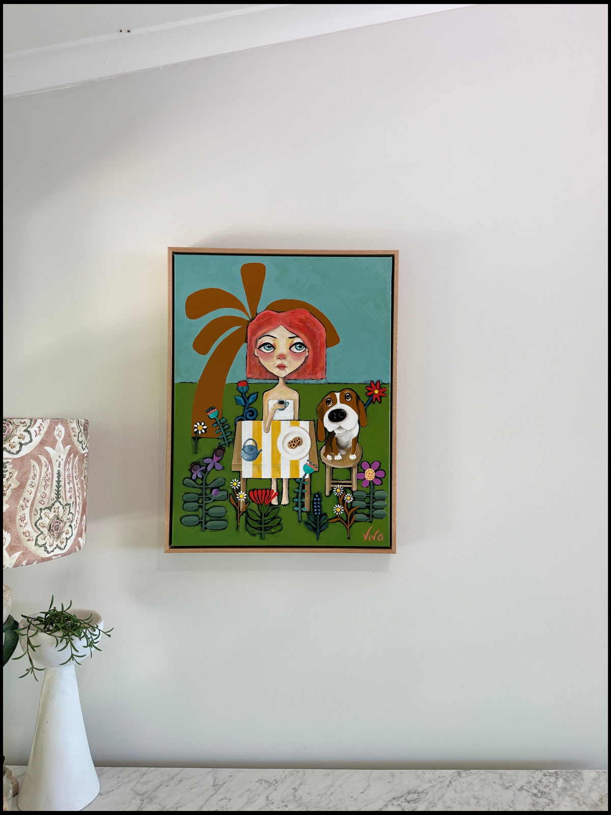 Framed artwork of a girl with red hair and a dog on a white wall.