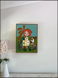 Framed artwork of a girl with red hair and a dog on a white wall.