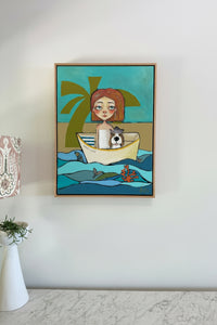Framed artwork of a woman with a dog in a boat on a beach scene, hanging on a white wall.