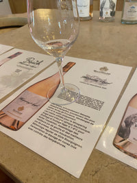 Wine glass being filled with white wine on a table with a wine label and bottle in the background.