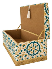 An open decorative storage box with a tan fabric interior, gold-tone support rods, a cream tassel, and embroidered exterior detailing in teal and gold on a white base, shown against a black background.