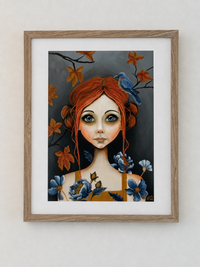 Framed artwork of a woman with red hair and blue flowers on a white wall